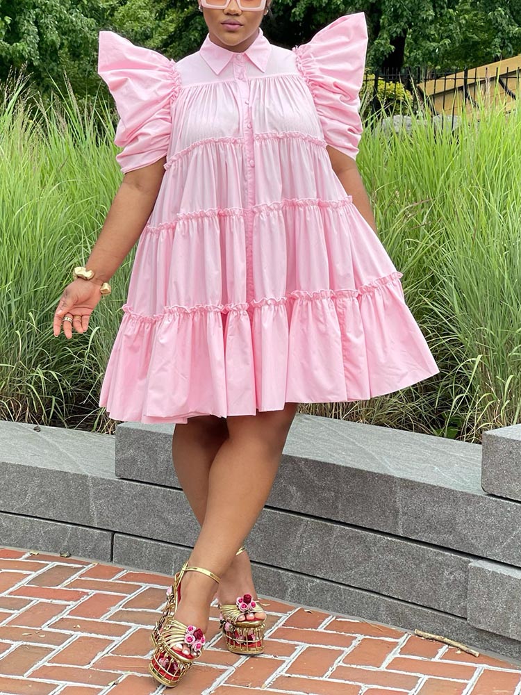 Woman wearing a pink tiered puff sleeve collared dress with a button-down front and gold platform heels.