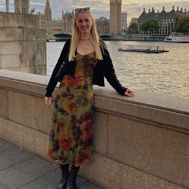 Woman posing by a river wearing a floral print midi slip dress and a black cardigan.