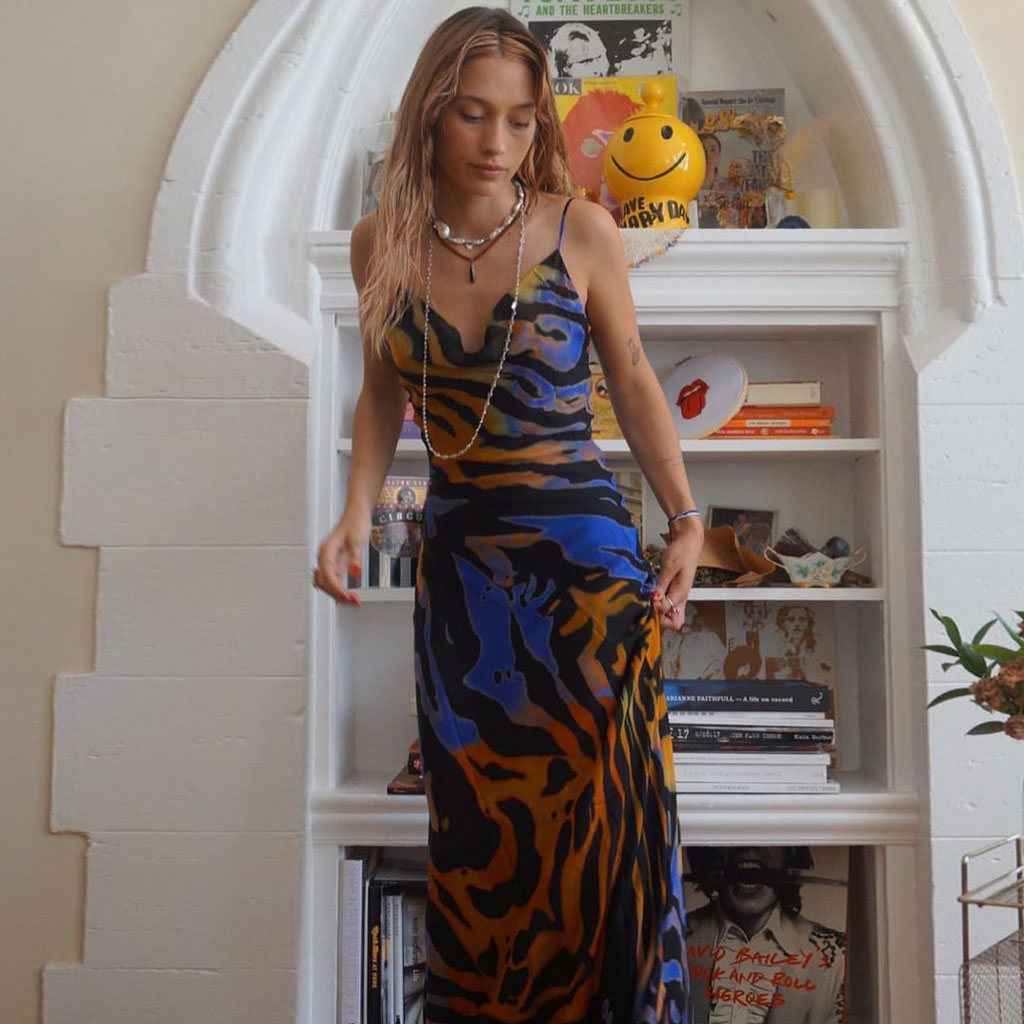 Woman wearing a printed maxi dress standing in front of a bookshelf.