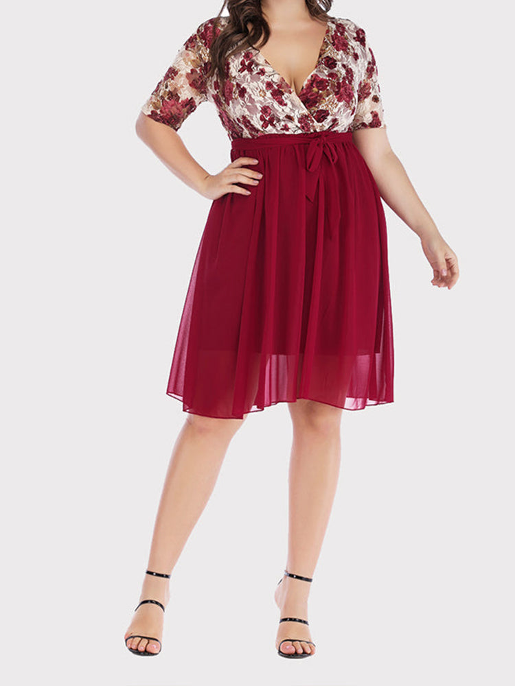 Full body shot of a plus size woman in a burgundy floral print lace wrap dress and black heels