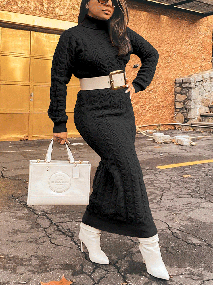 Woman posing in a black cable knit turtleneck maxi dress with a white belt and white boots, holding a white handbag.