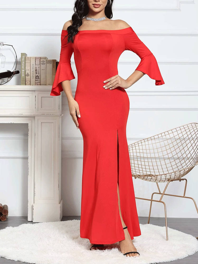 Woman wearing a red off-the-shoulder mermaid gown with bell sleeves and a high slit, standing in a room with a fireplace and chair.