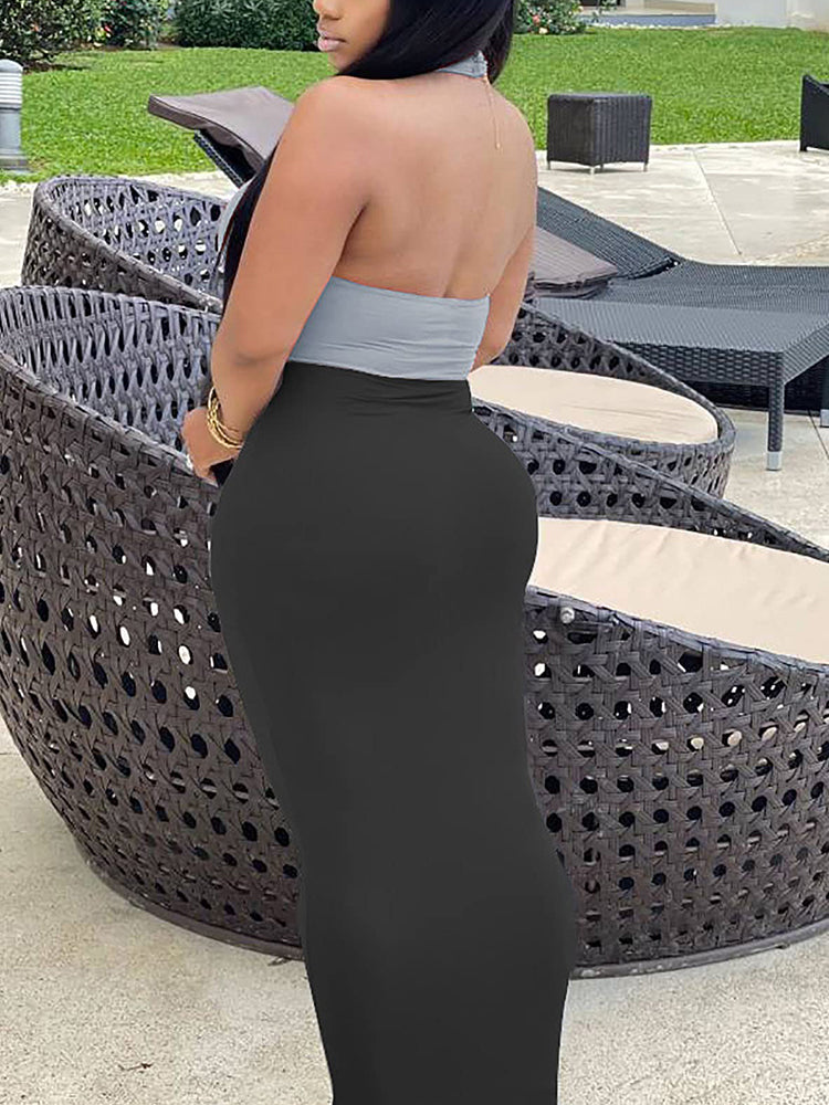 Rear view of a woman wearing a light grey halter crop top with a knot detail and a black maxi skirt.